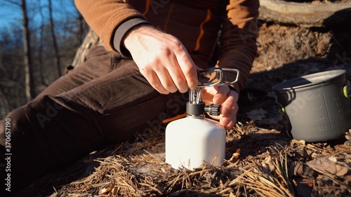 The theme of tourism is hiking and traveling in nature. Hands A Caucasian man uses equipping to cook food outside. A tourist installs a stove burner on a balloon cartridge with gas for boiling water