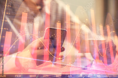 Double exposure of man's hands holding and using a phone and financial graph drawing. Analysis concept.