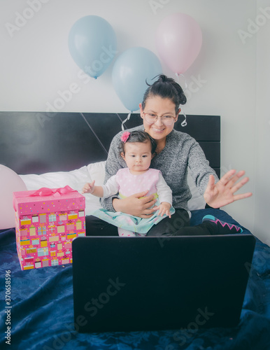 Madre y su bebé felices celebrando el cumpleaños a través de internet durante la cuarentena por Covid. Madre e hija celebran el cumpleaños en asilamiento usando la computadora.