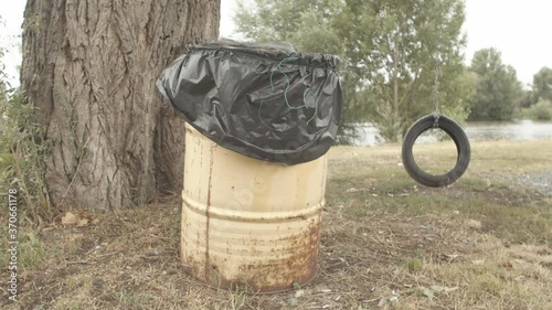 Trash can lonely tire swing near riverbank in Melnik, wide angle photo