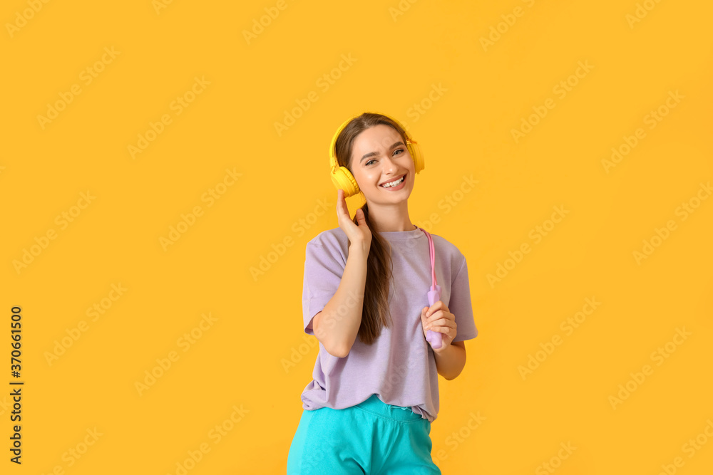 Sporty young woman with headphones and jumping rope on color background Sporty young woman with headphones and jumping rope on color background