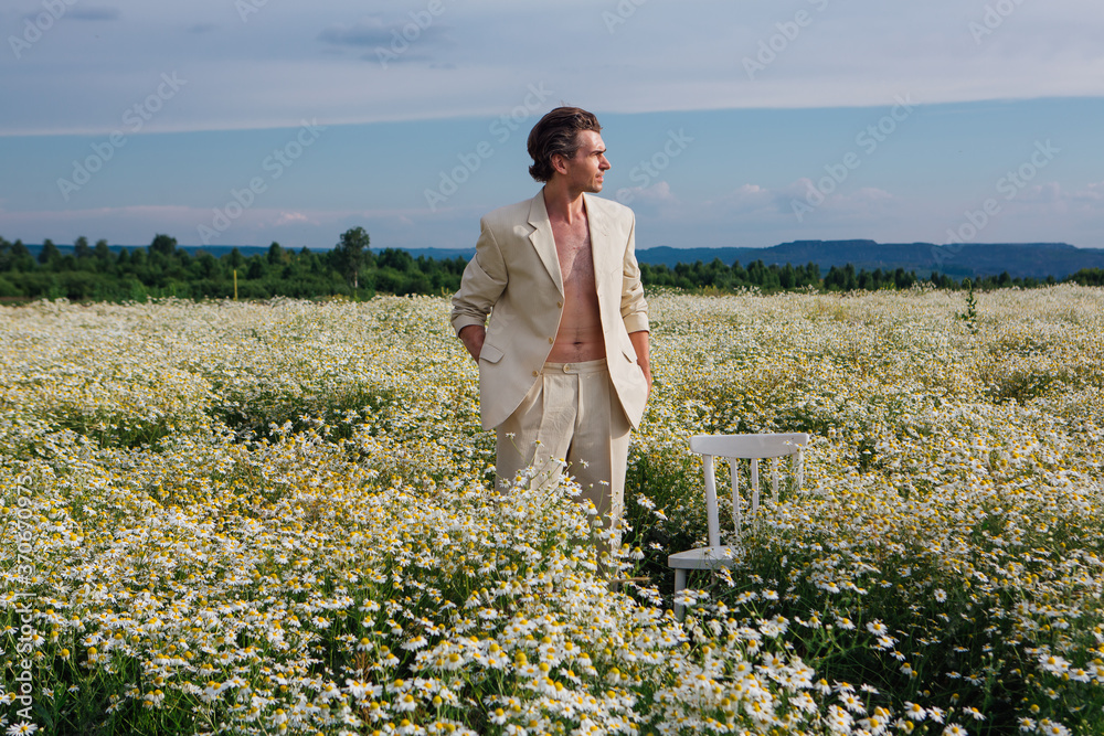 Tall handsome man standing in camomile flowers field