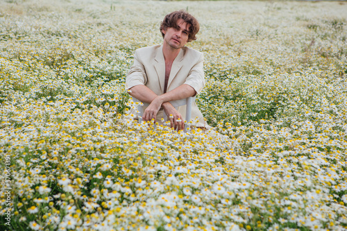 Tall handsome man sitting on a white chair in camomile flowers field