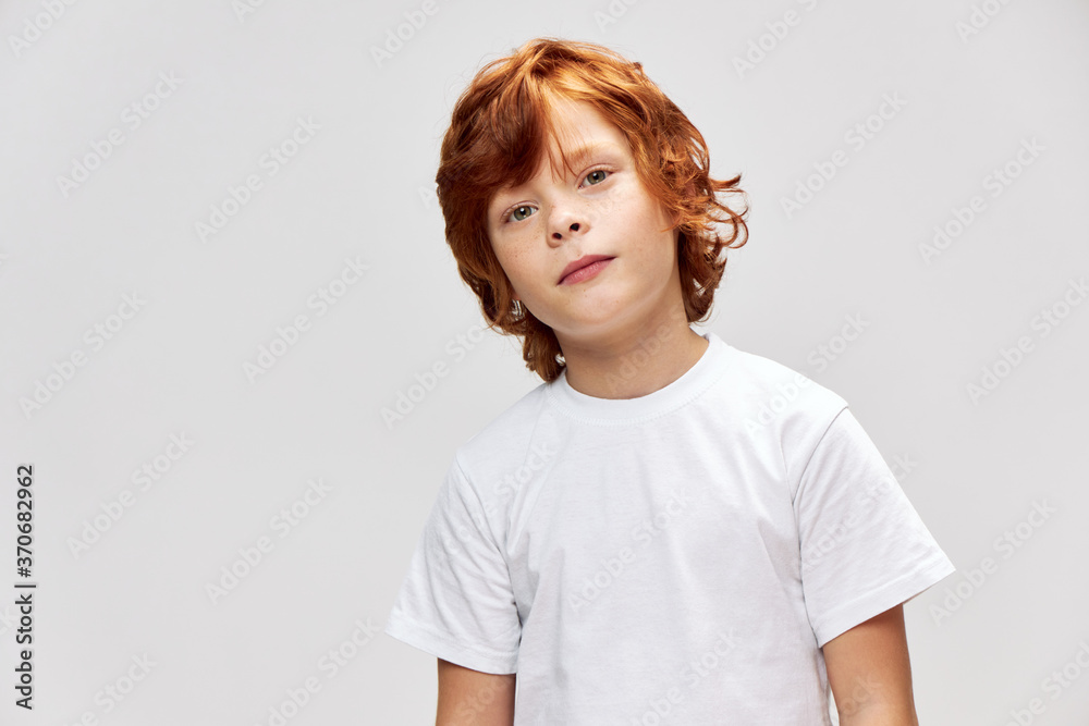 Red haired child in a white t-shirt tilted his head to one side red Red haired child in a white t-shirt tilted his head to one side red