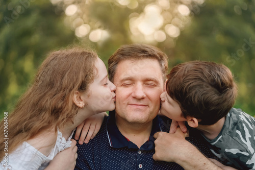 Little boy and girl kissing his dad on cheek.