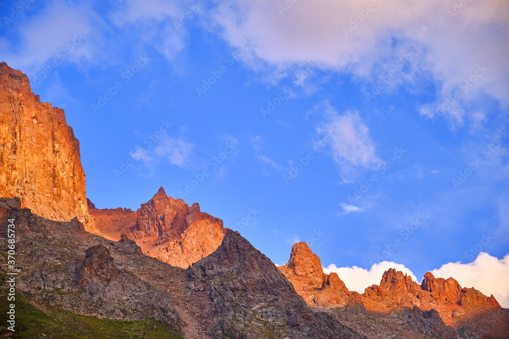 Huge cliffs on the background of blue sky with clouds in the light of setting sun; majestic mountain view at sunset