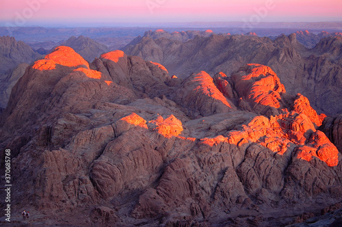 Fototapeta Naklejka Na Ścianę i Meble -  Early morning view from the top of Mount Moses at Sinai mountains in Egypt; delightful sunrise with the first rays of the sun on the rocks and the figures of tourists for scale