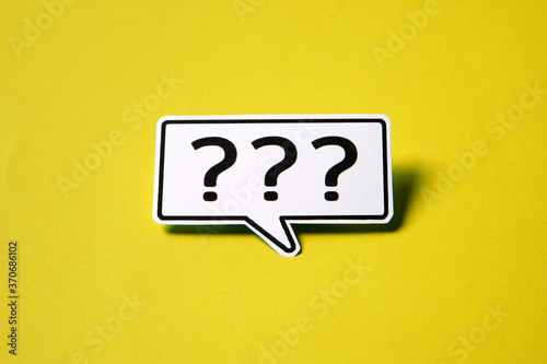Three question mark speech bubble on white paper isolated on yellow paper background with drop shadow.