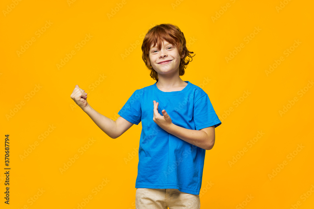 boy red hair blue t-shirt yellow isolated background freckles fight show fist to the side boy red hair blue t-shirt yellow isolated background freckles fight show fist to the side