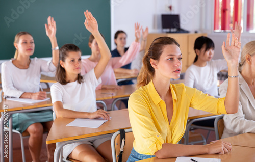 Group of young women studying together in classroom, raising hands to answer © JackF