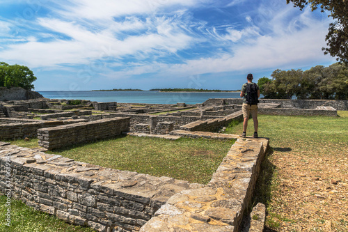 A tourist with a backpack standing of the top of roman ruins enjoying the view on the Adriatic sea at Brijuni national park, in Croatia. photo