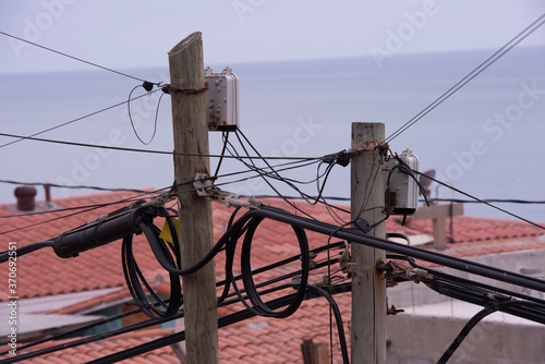 Power lines on a wooden post with Spanish tiled roofs in the background.