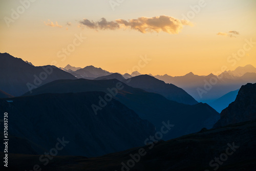 Colorful dawn landscape with beautiful blue mountains silhouettes and golden gradient sky with clouds. Vivid mountain scenery with picturesque multicolor sunset. Scenic sunrise view to mountain range. © Daniil