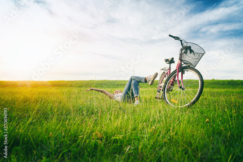 Happy free summer time. A woman lies on the grass on a green field next to a bike. Summer Country Vacation and Adventure Concept