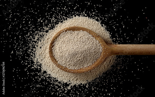 Active dry yeast granules pile with wooden spoon isolated on black background and texture, top view with clipping path photo