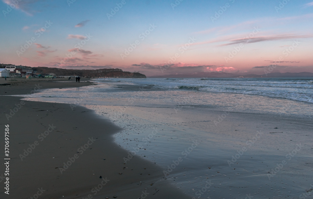 Sea with waves, sea foam and sandy beach at dusk