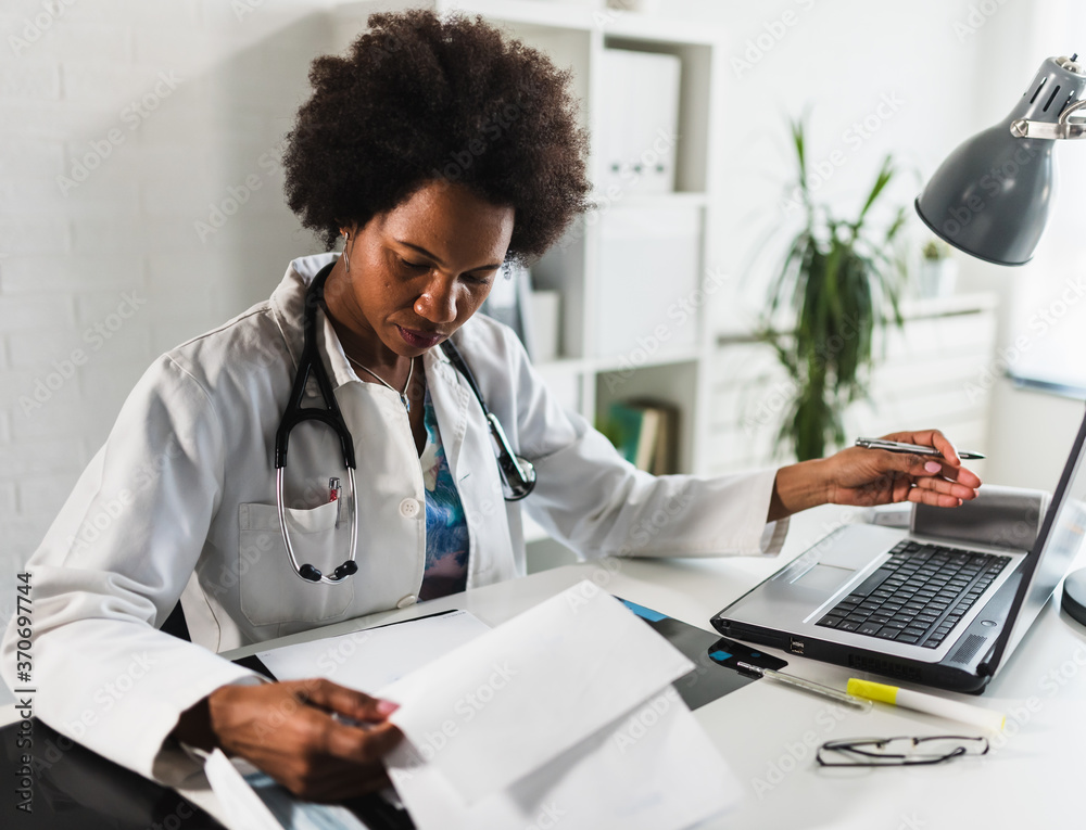 © lordn - Woman doctor with stethoscope looking at medical papers at her office working hard