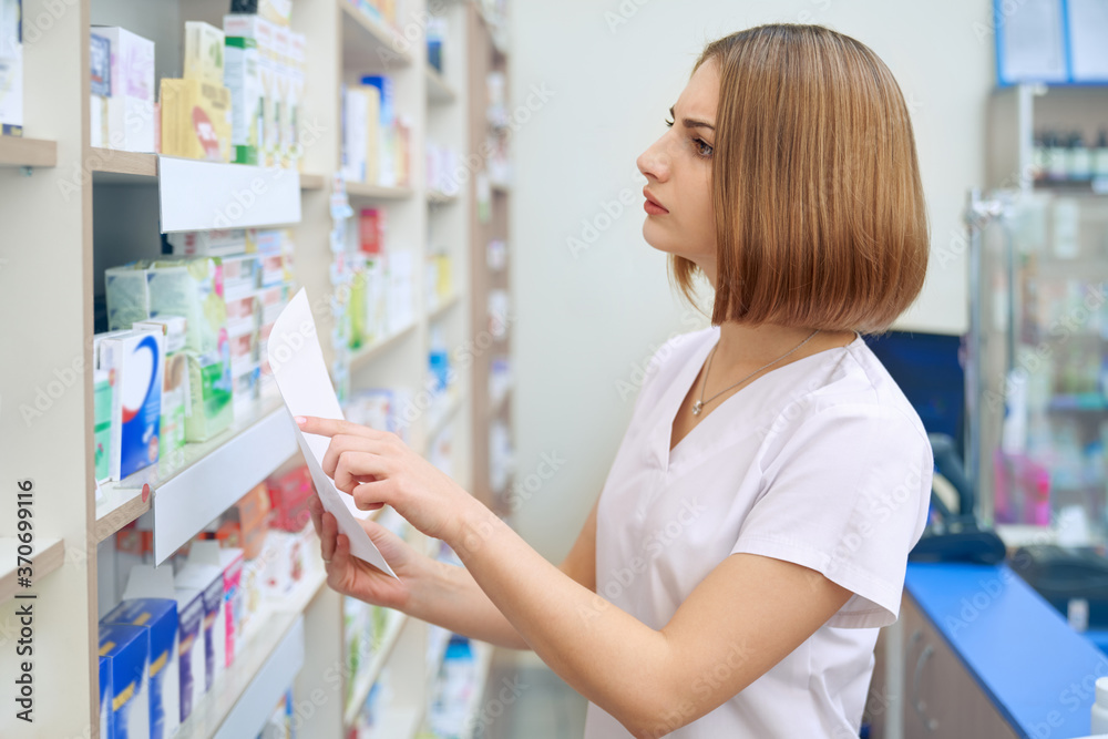 Female pharmacist searching for medicaments from prescription.
