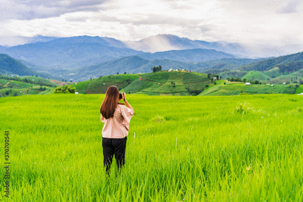 Young woman traveler on vacation taking a picture at beautiful green rice terraces field in Pa Pong Pieng, Chiangmai Thailand