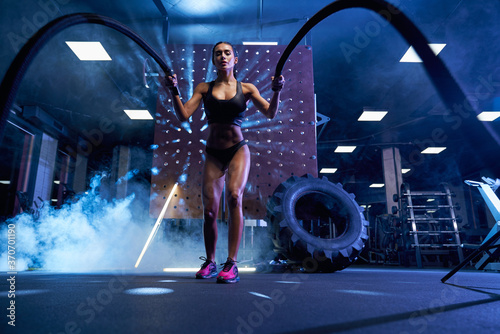 Muscular young woman training with ropes.