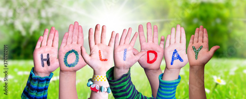 Children Hands Building Colorful English Word Holiday. Sunny Green Grass Meadow As Background