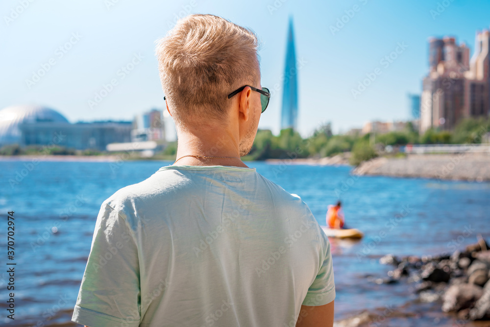 A young man with a backpack in Saint Petersburg on the Gulf of Finland with a view of business centers and the Lakhta Center skyscraper