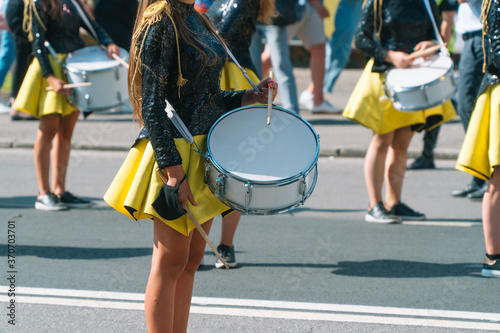 Street performance of festive march of drummers girls in yellow black costumes on city street. Street music concept
