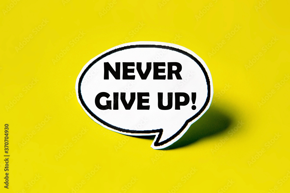 Never give up speech bubble on white paper isolated on yellow paper background with drop shadow. COPY SPACE. Never give up speech bubble on white paper isolated on yellow paper background with drop shadow. COPY SPACE.
