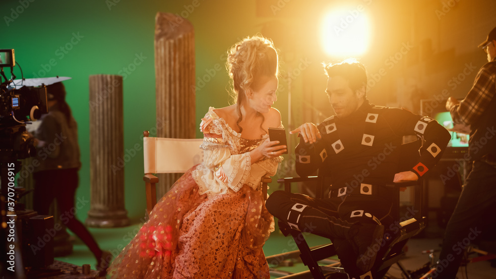 Φωτογραφία Beautiful Smiling Actress Wearing Renaissance Dress and Actor Wearing Motion Capture Suit Sitting on Chairs Share Social Media Posts via Smartphone