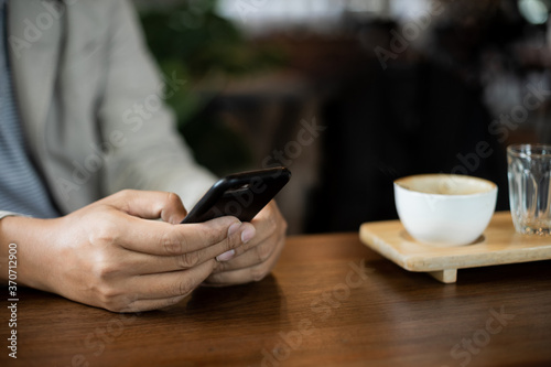 Close up of businessman's hands holding and typing on black cellphone for business communication in the cafe with a cup of coffe on wooden table. Business stock photo.