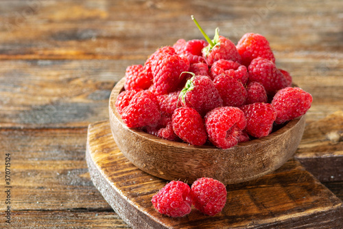 Raspberries in a wooden bowl on a brown wooden table. Raspberry berry close-up. Fresh raspberries in a plate. Space for text. Healthy diet