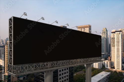 Blank black road billboard with Bangkok cityscape background at sunset. Street advertising poster, mock up, 3D rendering. Side view. The concept of marketing communication to promote or sell idea.