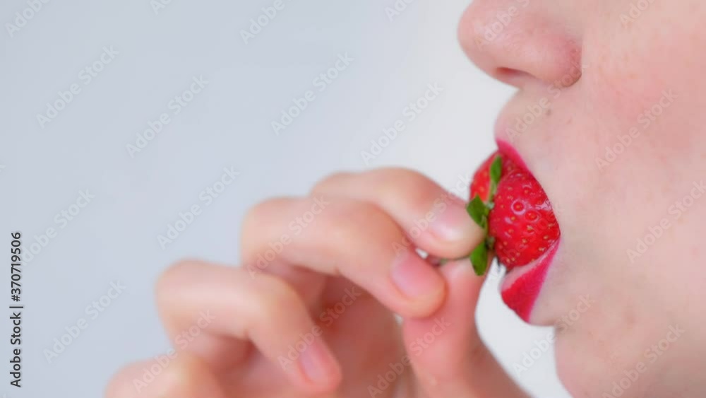 Woman with sensual red lips is eating strawberry on white background, lips closeup, side view. She has a freckles on her face. Vitamins from fresh strawberry. Unrecognizable sexy young girl. Woman with sensual red lips is eating strawberry on white background, lips closeup, side view. She has a freckles on her face. Vitamins from fresh strawberry. Unrecognizable sexy young girl.