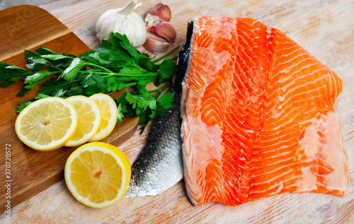Background with appetizing raw salmon fillet with lemon and greens before cooking