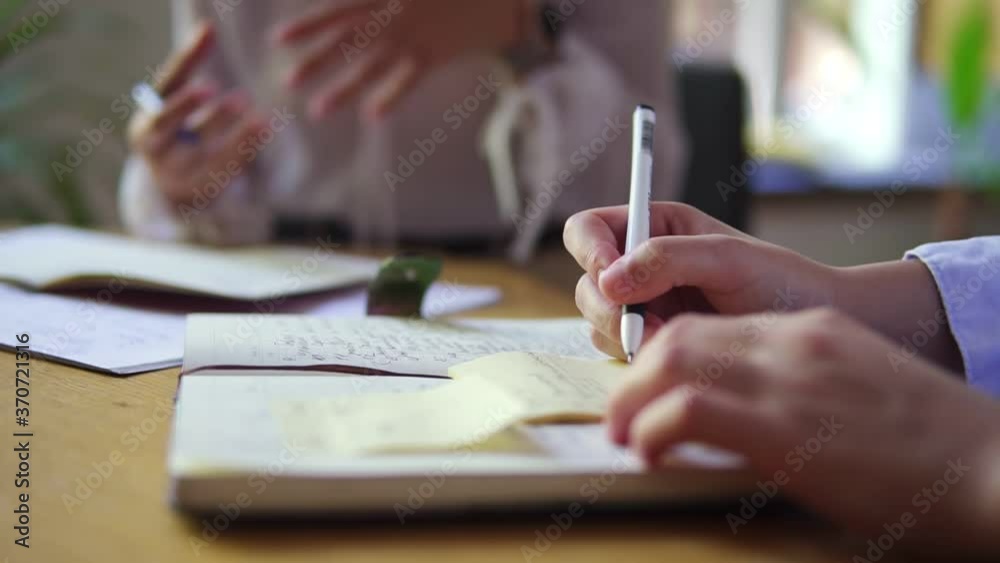 A female hand writing notes in notepad. Writing down business ideas. Closeup of business woman hand write notes. Unrecognizable woman gesturing on background A female hand writing notes in notepad. Writing down business ideas. Closeup of business woman hand write notes. Unrecognizable woman gesturing on background