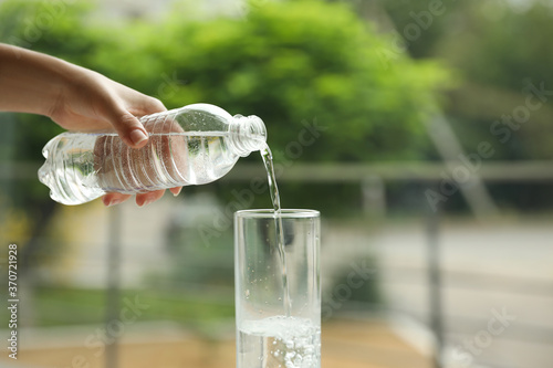 Woman pouring water from bottle into glass against blurred background, closeup