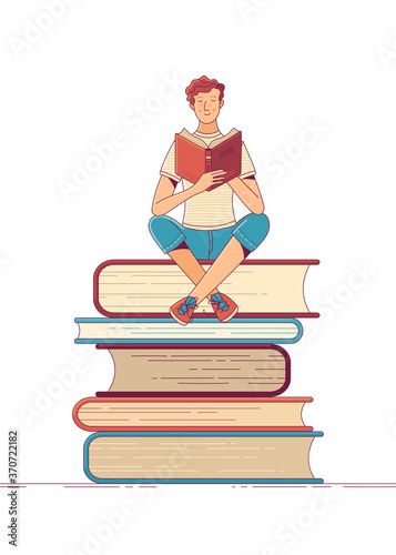 Young man reading book while sitting on stack of books