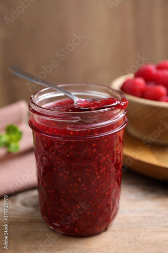 Delicious raspberry jam in jar on wooden table, closeup