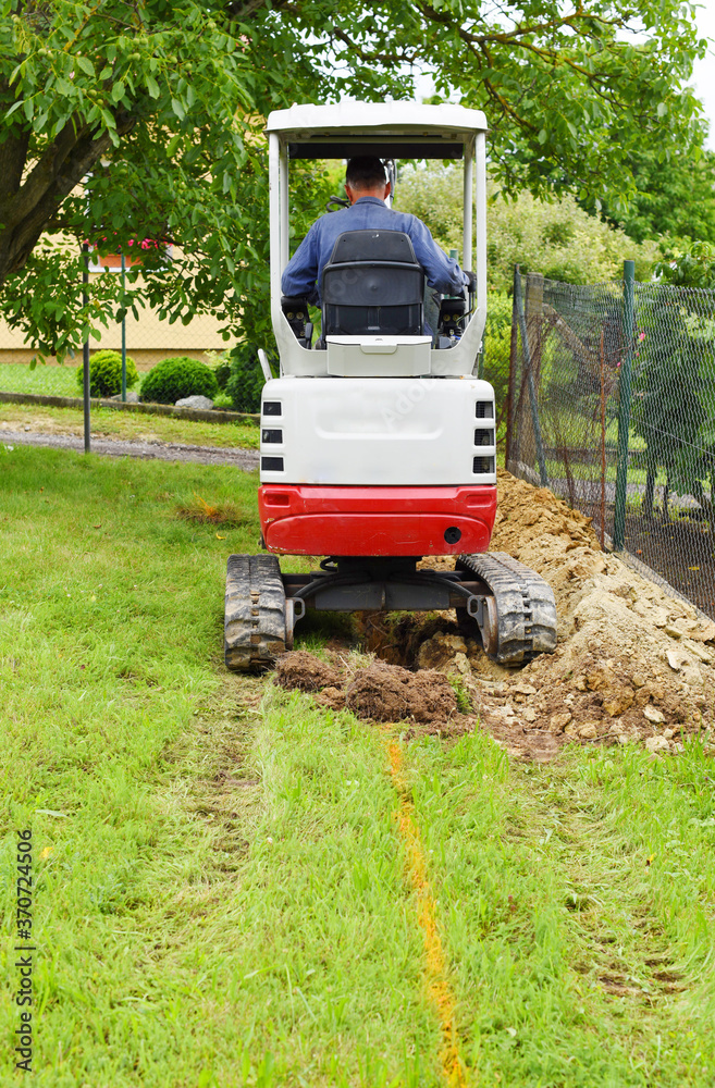 Workman using a mini digger to excavate a hole in the garden. Czech republic, Europe.