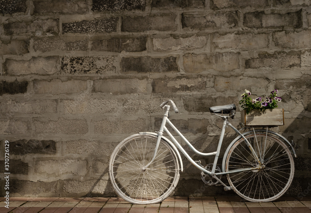 Vintage white bicycle on a background of a concrete wall with one box of flowers. Right location.