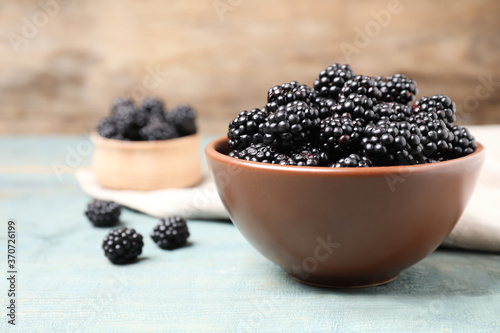 Fresh ripe blackberries in bowl on blue wooden table. Space for text