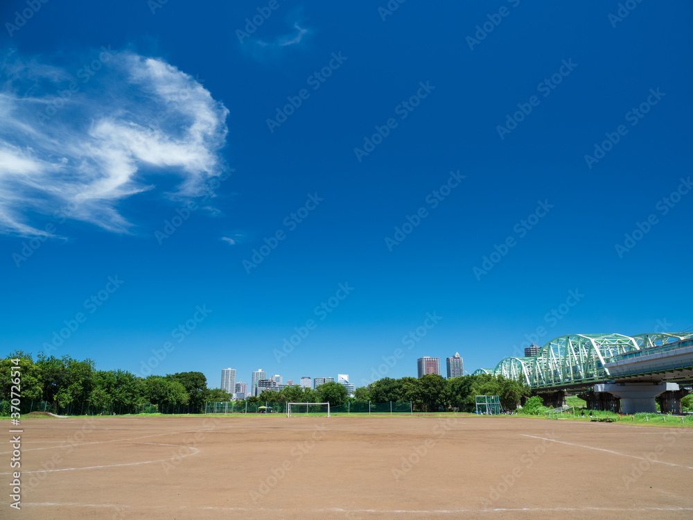 Fototapeta premium 真夏の青空と土のサッカーコートの風景