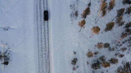 Aerial view of car driving on winter road passing woods and trees getting to wanderlust destination, bird's eye view of road trip on 4x4 trip driving on off road for discover journey
