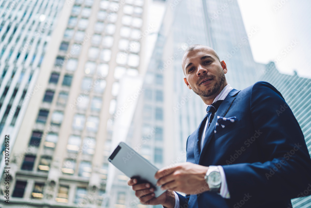 Portrait of self-confident male owner of business standing outdoors with tablet in business district with skyscrapers, serious entrepreneur checking notification on portable pc using 4G connection. Portrait of self-confident male owner of business standing outdoors with tablet in business district with skyscrapers, serious entrepreneur checking notification on portable pc using 4G connection.