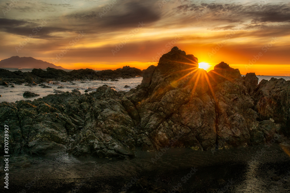 Spectacular Sun flare between the crevice in the rocks at dawn on the Kaikoura Coast