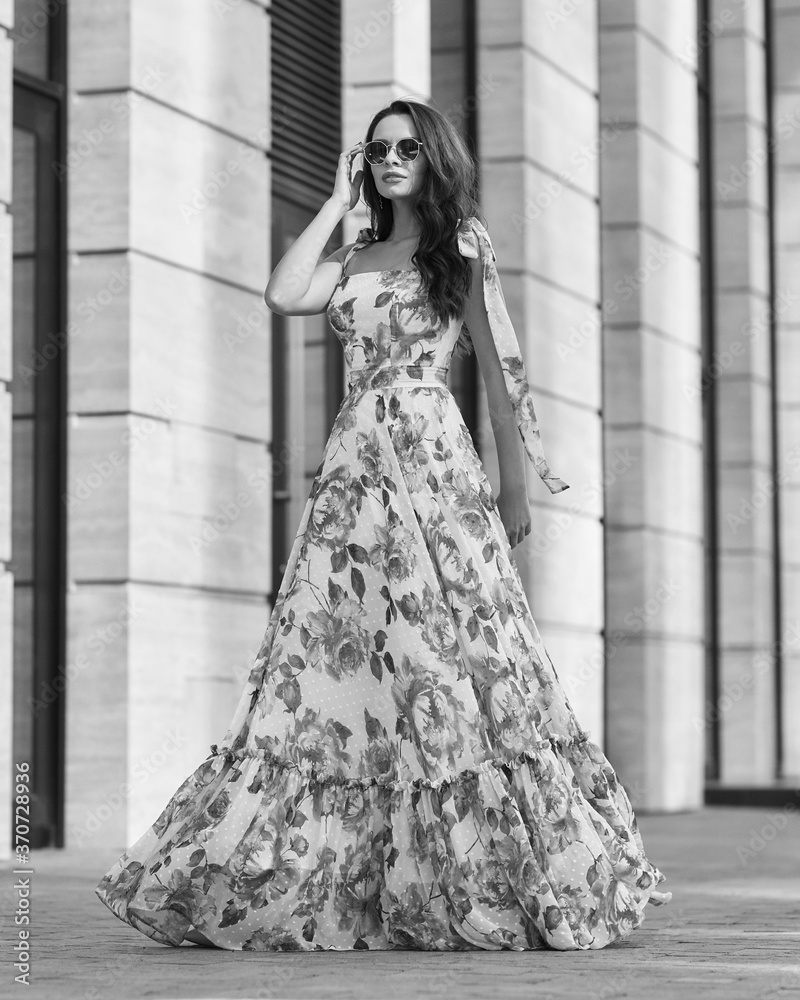 Elegant woman in long pink summer dress with floral print walking at city street. Outdoor full length portrait. Pretty female model Elegant woman in long pink summer dress with floral print walking at city street. Outdoor full length portrait. Pretty female model