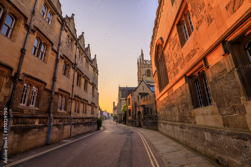 Merton Street, a side alley, in Oxford at sunrise with no people around, early in the morning on a clear day with blue sky. Oxford, England, UK.