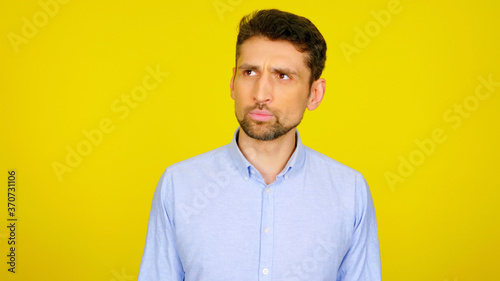 Handsome bearded man looks away on yellow background with copy space. Guy in light blue shirt looks in place for text or goods