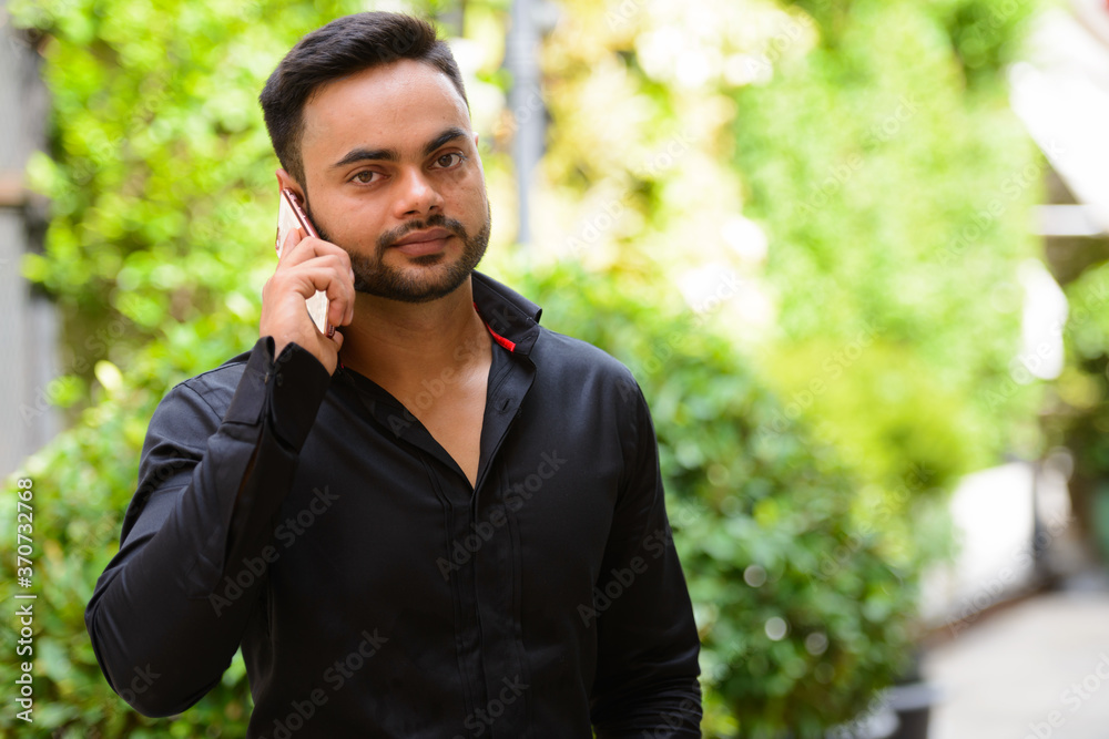 Young handsome bearded Indian businessman talking on the phone at the park Young handsome bearded Indian businessman talking on the phone at the park