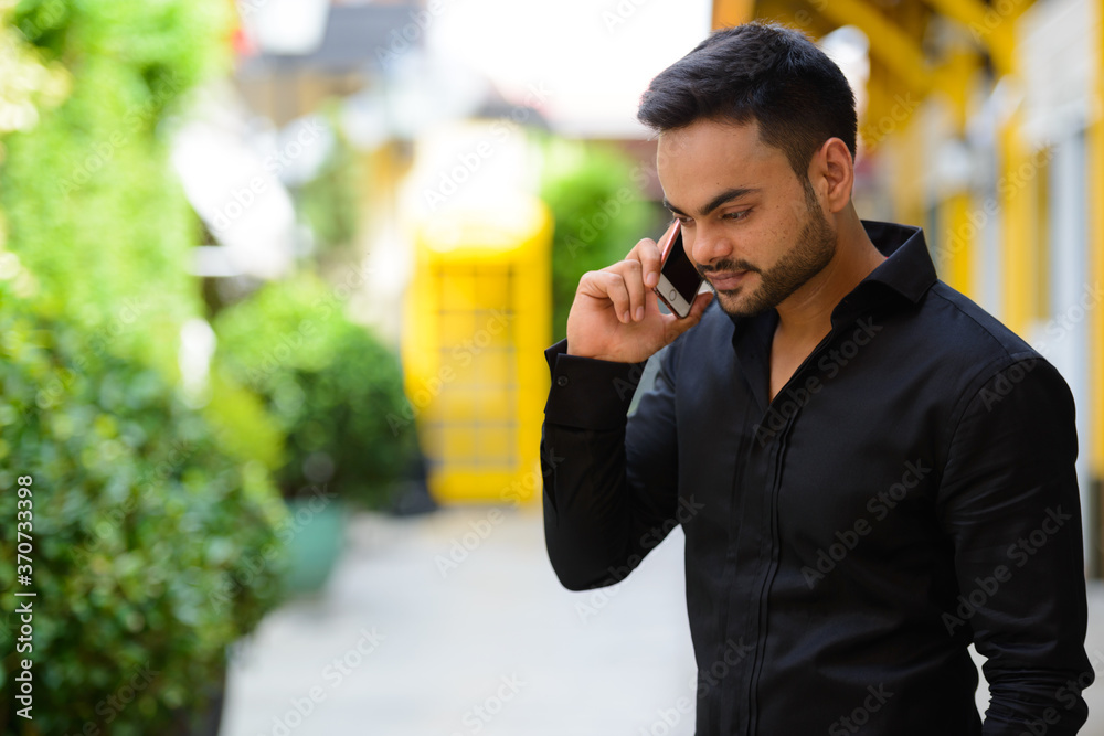 Young handsome bearded Indian businessman talking on the phone at the park Young handsome bearded Indian businessman talking on the phone at the park
